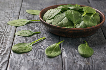 Spinach leaves neatly arranged near a clay bowl on a wooden table. Food for fitness.