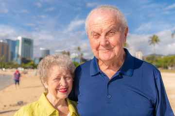 Close up wide angle view of a beautiful senior couple posing for a portrait while visiting Honolulu Hawaii, at the Ala Moana beach, with the skyline in the distance.