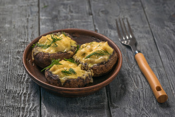 Three baked mushrooms with chicken breast and cheese in a clay bowl on a wooden table.