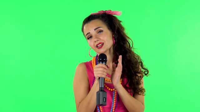 Girl sings into a microphone and moves to the beat of music. Green screen