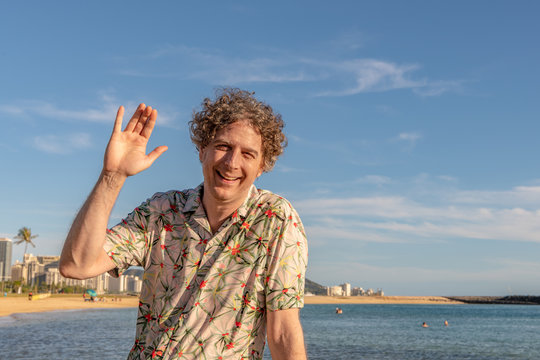 A middle aged man waves at the camera while enjoying the day at the beach, in Honolulu, Hawaii. Man on left side of photo.