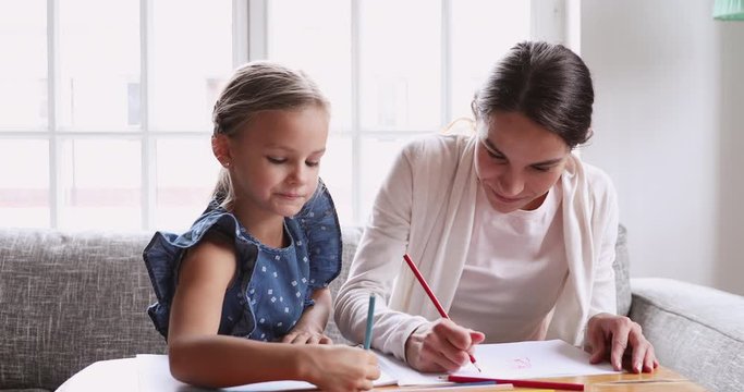 Young nanny teaching primary school girl drawing pencils together