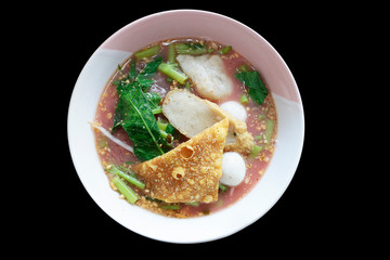 Thai-style noodle soup with fishballs, crispy wonton skin, on black background.