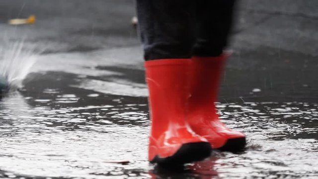 Detail of red rubber  rainy bots jump on muddy splashing water, freedom, slow motion, conceptual, little child own rules