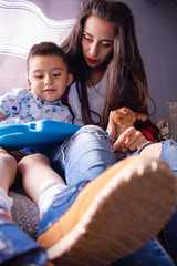 Young mother, her child and her pet sitting on a sofa playing games using a digital tablet at home