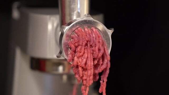 Minced meat (Ground meat) coming out from the grinder. Dark background.
