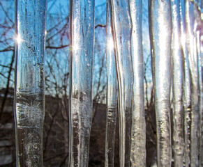 Icicles against the blue sky. Transparent clear ice shining in the sun in winter or spring day. Frozen water in the form of long icy cone-shaped.