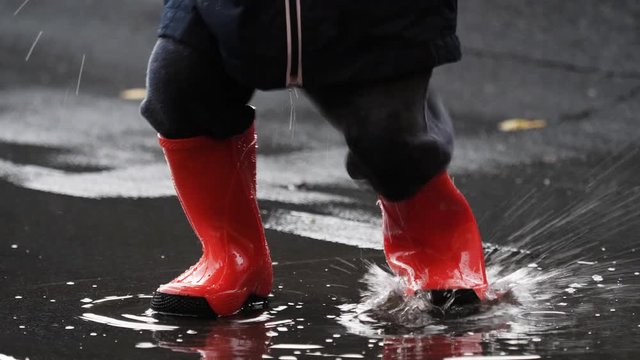 Detail of child rubber red boots jumping on rain puddle