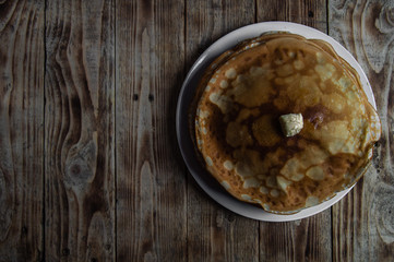 Pancakes with a piece of butter on a white plate on a wooden table