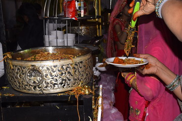 Hand of Indian woman carrying Fried Noodless in his plate by a spoon from a large pot