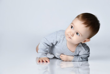 Little baby boy toddler in grey casual jumpsuit and barefoot lying on floor, smiling and looking up