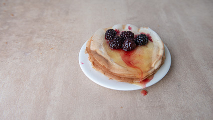 Stack of thin pancakes poured with honey and decorated with fresh blueberries side view with selective focus and light background with copy space