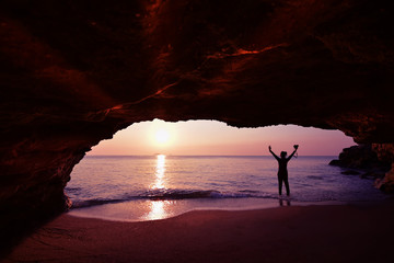 Silhouette of woman standing using camera to take a picture in front of the cave in the morning