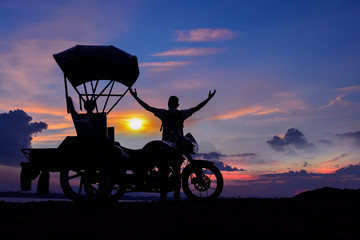A man with a motorcycle with a roof standing watching the sunset
