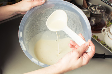 Girls hand is picking up mixture from large cup for baking pancakes.