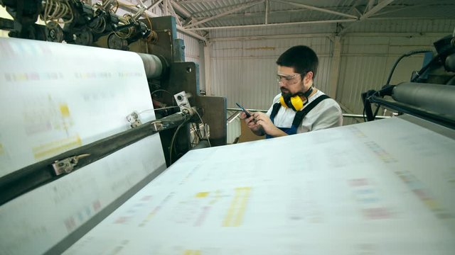 Male worker with a smartphone is observing rolling paper