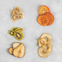 Healthy homemade fruit chips from apple, persimmon, pear, kiwi and banana on grey background. Organic diet food. The vegan diet. Dried fruits. Vegetarian plant based snack concept. Top view.