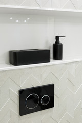 Economic toilet black flush press with two separate buttons for flushing toilet. Shelf with black bathroom accessories.