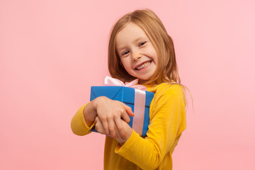 My best present! Delighted charming little girl embracing gift box and smiling joyfully to camera, satisfied with birthday surprise, her child dream come true. studio shot isolated on pink background