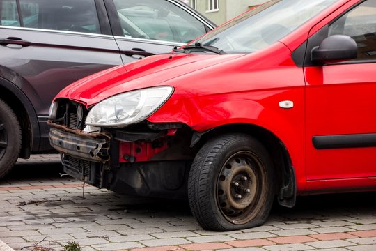 A small red Hyundai Getz hatchback car with missing frontal par after a traffic accident with cooler, radiator visible and punctured tyre.