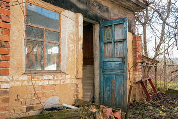 Retro-styled abandoned brick barn or farmhouse with open blue doors and big window in village or countryside. Close-up.