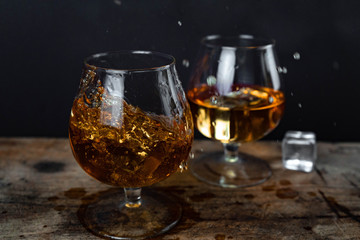 Two whiskey / cognac glasses with ice on a wooden background. Dark backdrop.