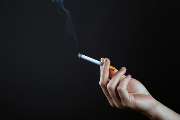 female hand holding a smoking cigarette on a dark background copy space. harm from smoking cigarettes