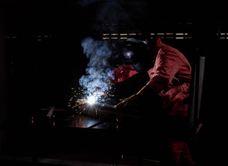 A man wearing safety mask and suit is welding metal