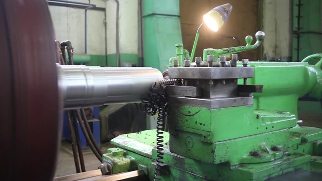 A metal round billet rotates in a lathe and is machined by a turning tool. Metal shavings fly off the workpiece.