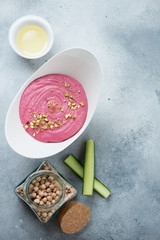 Hummus with addition of beetroot over light-blue stone background, flatlay with copy space, vertical shot