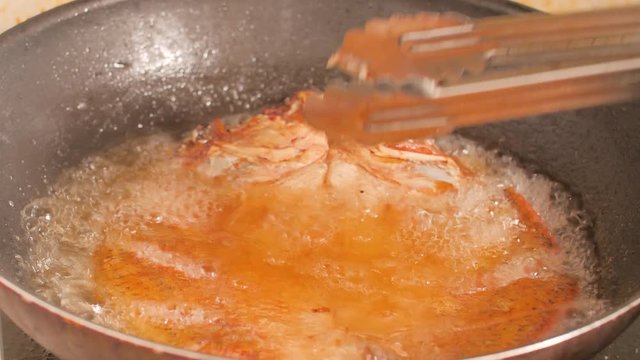 Turn the snapper to fry in a black pan and the hot oil is boiling.