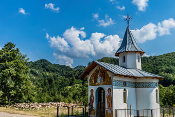 Small church on the side of the road with wooden logs puffy clouds and forest in the background