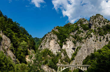 Mountain bridge passing through mountain forest with mountains and puffy clouds in the background