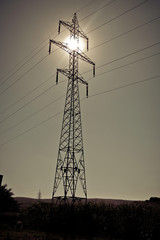 Sun shining through high voltage power lines on power pylon