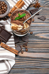 Classic tiramisu dessert in a glass cup and pieces of chocolate on wooden background