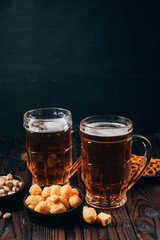Beer and appetizing snacks. table with two mugs of craft lager and salty traditional appetizers. Finger food. Oktoberfest food, pub concept