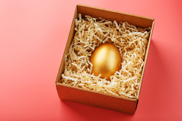 Egg made of gold in a wooden box on a pink background. The concept of exclusivity and superprize. Minimalistic composition.