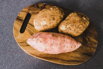 healthy organic food ingredients, potatoes and sweet potato on cuttin board on kitchen counter