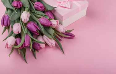 a bouquet of pink tulips and a gift box for women's day on a pink background. Mother's day greetings