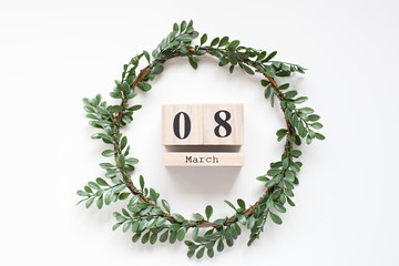 Spring wreath of green leaves with a wooden calendar on white background. Wooden block calendar. Concept International Women's Day. Spring composition of green leaves. Flat lay, top view, copy space. 