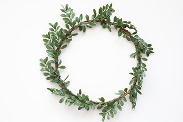 Green wreath with leaves on white background. Wreath made of branches. Flat lay, top view, copy space. Spring composition. Flowers composition. Easter. Boxwood wreath for Christmas. Scandinavian style - obrazy, fototapety, plakaty