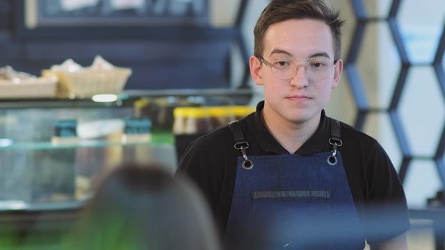 skilled waiter in apron takes order from regular visitors standing against cafe window-case closeup slow motion