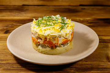 Tasty layered salad with potatoes, chicken breast, marinated mushrooms, carrots, eggs and mayonnaise on wooden table