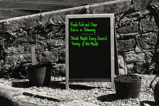 Menu Outdoord On A Blackboard  With Green Writing Advertising Fish And Chips And Steak Night For A Pub, Restraunt, Cafe.  With Selective Colour