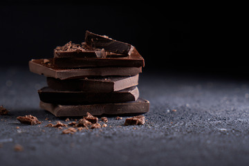 Piece of dark chocolate and chocolate chips on a dark background