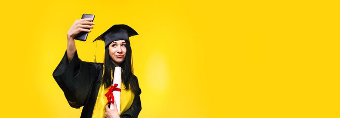 graduate woman makes selfie photo on phone over yellow background, concept of successful completion...