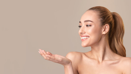 Woman Posing Holding Invisible Object On Hand Over Beige Background