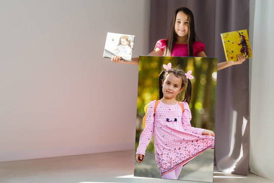 Cute little girl holding photo canvas at home