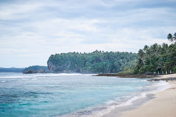 Beautiful landscape with white sand tropical beach, cloudy sky and green palm trees.