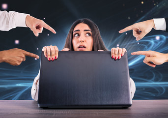 Afraid girl hides herself rear the laptop. She is victim of cyberbullying